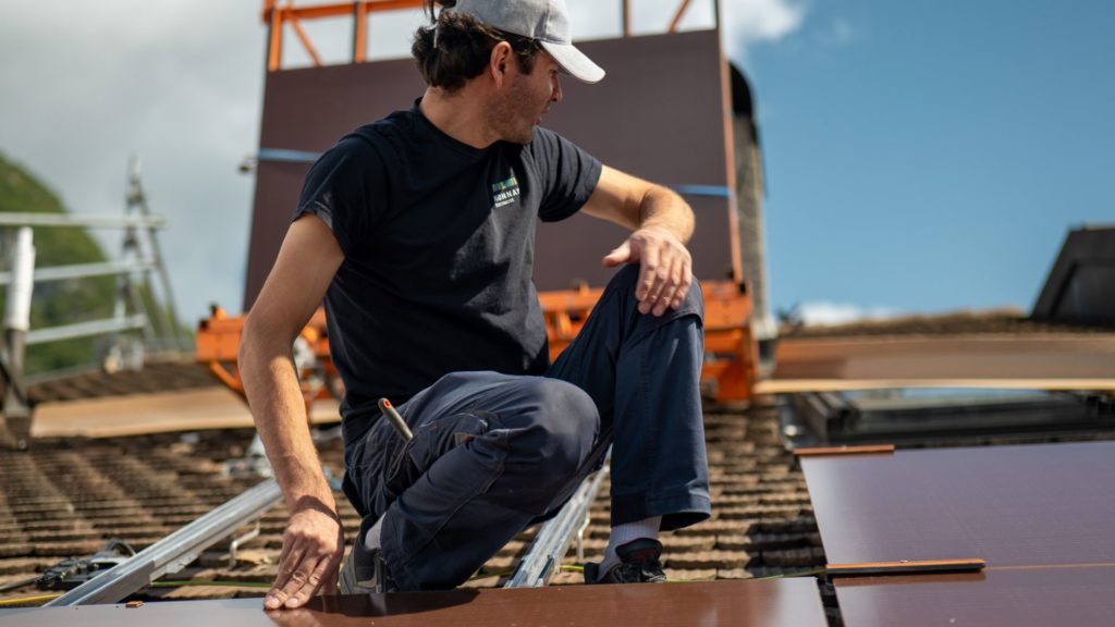 Technicien Monnay Électricité posant des panneaux solaires Megasol sur une toiture à Aigle.